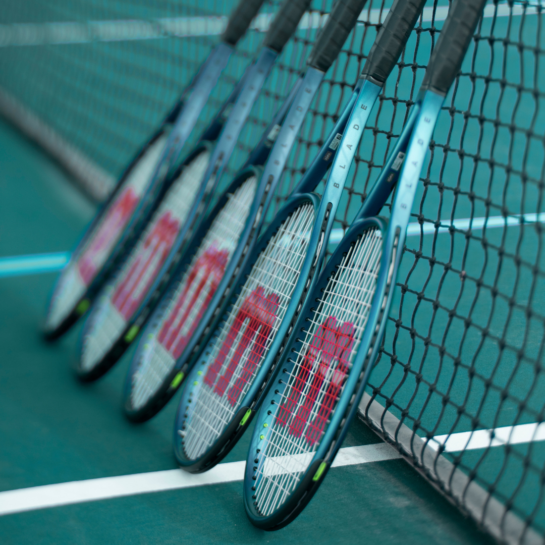 Die neuen Blade v9 sind auf einem türkisen Hardcourt-Tennisplatz gegen das Tennisnetz gelehnt.